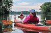 Kayakers paddling red canoes on a calm river with trees along the banks.