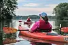 Kayakers paddling red canoes on a calm river with trees along the banks.