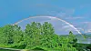 Rainbow arching over green trees beneath a blue sky.