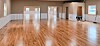Empty hall with wood floors, beige walls, windows, and a person bending near the right side.