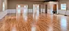 Empty hall with wood floors, beige walls, windows, and a person bending near the right side.