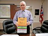 Man holding a stack of colorful folders behind a desk in an office.