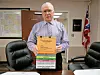 Man holding a stack of colorful folders behind a desk in an office.