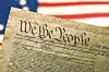 Close-up of a U.S. Constitution page over a blurred American flag.