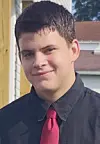 Young man wearing a black shirt and red tie standing outdoors near a house.