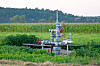 Industrial equipment installed in a green crop field with trees and hills behind it.
