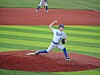 Baseball pitcher in blue and white uniform throwing a pitch on a striped field.