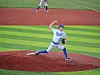 Baseball pitcher in blue and white uniform throwing a pitch on a striped field.