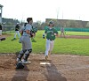 Youth baseball runner approaches home plate while a catcher in gray protective gear stands nearby.