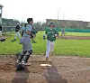 Youth baseball runner approaches home plate while a catcher in gray protective gear stands nearby.