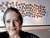 Woman in the foreground with a wall of small framed images arranged behind her.
