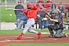 Softball batter in red swings while catcher kneels behind home plate.