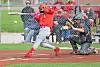 Softball batter in red swings while catcher kneels behind home plate.