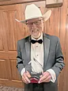 Man in a white cowboy hat and tuxedo holding a glass award indoors.