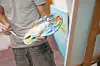 Person holding a paint palette with colorful paint and a brush in a studio.