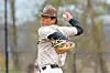 Baseball pitcher in a brown cap and white uniform mid-pitch on the mound.
