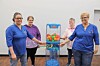 Four people stand beside a blue toy vending machine filled with colorful balls.