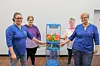 Four people stand beside a blue toy vending machine filled with colorful balls.