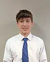 Young man in a white shirt and blue tie standing against a gray wall.
