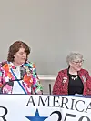 Two women stand behind a banner reading America 250 at a public event.
