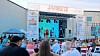 Crowd seated outdoors facing a lit stage with several performers.