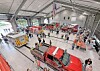 Fire trucks and emergency vehicles displayed inside a hangar with people walking among them.