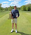 Golfer standing on a fairway holding two trophies on a sunny golf course.