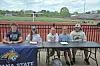 Several people seated at a table in front of a Montana State banner beside an outdoor sports field.
