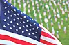 Close-up of an American flag with a blurred cemetery of white headstones behind it.
