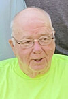 Close-up of an elderly man wearing glasses and a bright neon yellow shirt.