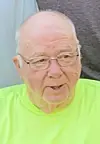 Close-up of an elderly man wearing glasses and a bright neon yellow shirt.