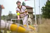 Softball player in a striped uniform reaching forward to field a ball on an outdoor field.