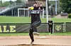 Softball pitcher in black uniform mid-throw on a dirt field during a game.