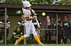 Player in striped uniform swings at a yellow ball during an outdoor game.