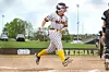 Softball player in striped uniform and yellow socks runs on a dirt field during a game.