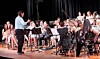 A conductor stands facing a seated orchestra performing on stage.