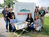 Several people pose outdoors beside a Gassaway sign and a small folding table with a display.
