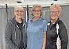 Three women standing side by side indoors and smiling at the camera.