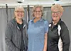 Three women standing side by side indoors and smiling at the camera.