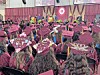 A crowded commencement ceremony with graduates in maroon caps and gowns seated indoors.