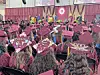 A crowded commencement ceremony with graduates in maroon caps and gowns seated indoors.