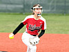 Softball pitcher in a red jersey and white pants throws a ball on a field.