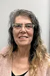 Close-up portrait of a smiling woman wearing glasses against a plain background.