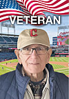 Elderly man in a tan cap and glasses posed in front of a baseball stadium with an American flag graphic and the word Veteran.