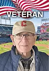 Elderly man in a tan cap and glasses posed in front of a baseball stadium with an American flag graphic and the word Veteran.