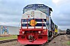 Blue and red freight locomotive on railroad tracks in a rural setting.