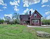 Red house with white trim on a grassy property beneath a partly cloudy blue sky.