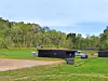 Outdoor grassy site with black containers, a blue utility vehicle, and a wooded hill in the background.