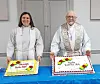 Two clergy members stand behind two decorated cakes on a blue table indoors.