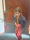 Child holding a pink ball while climbing an indoor stairway near a wooden door.